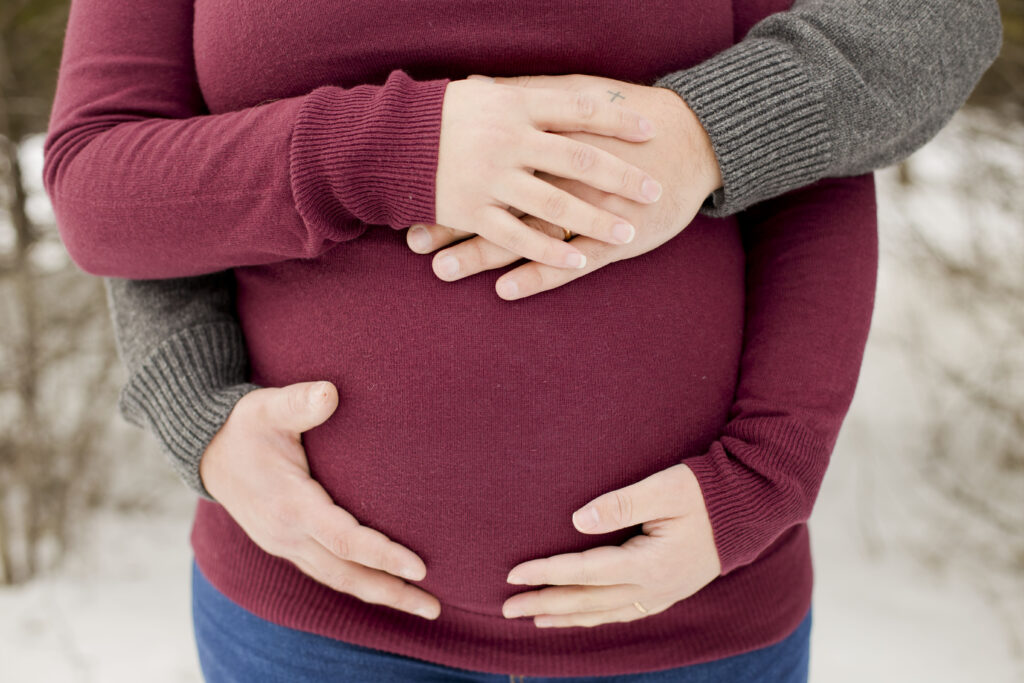 Pregnant belly embraced by mom and dad from an outdoor maternity session